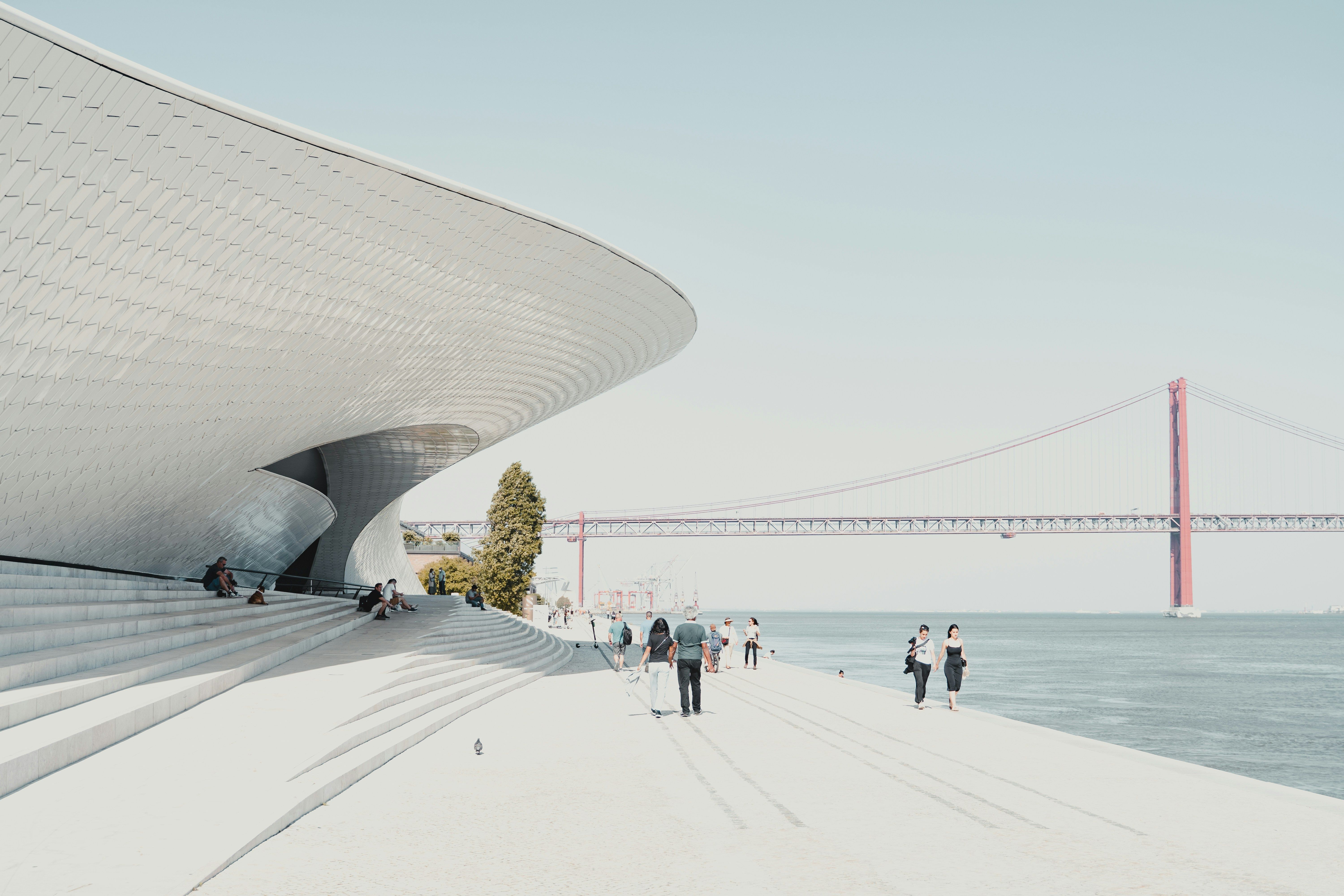 a group of people walking along the museum of art, architecture and technology of lisbon next to the Tagus river